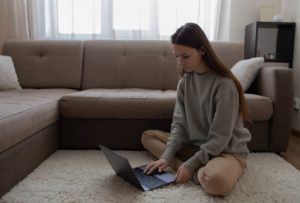 young woman sitting on the floor and typing on her laptop