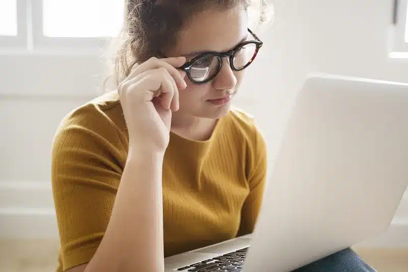 a girl wearing glasses looking at her laptop