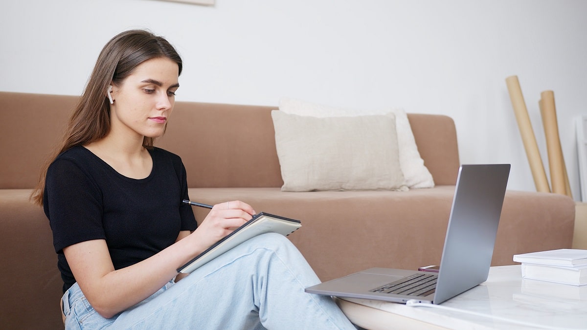 Positive woman using laptop and taking notes